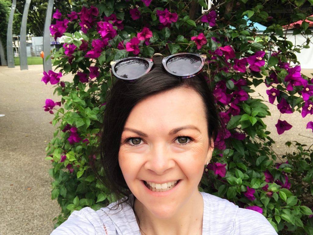 Rebecca smiling at the camera. Pink Bougainvillea in the background.